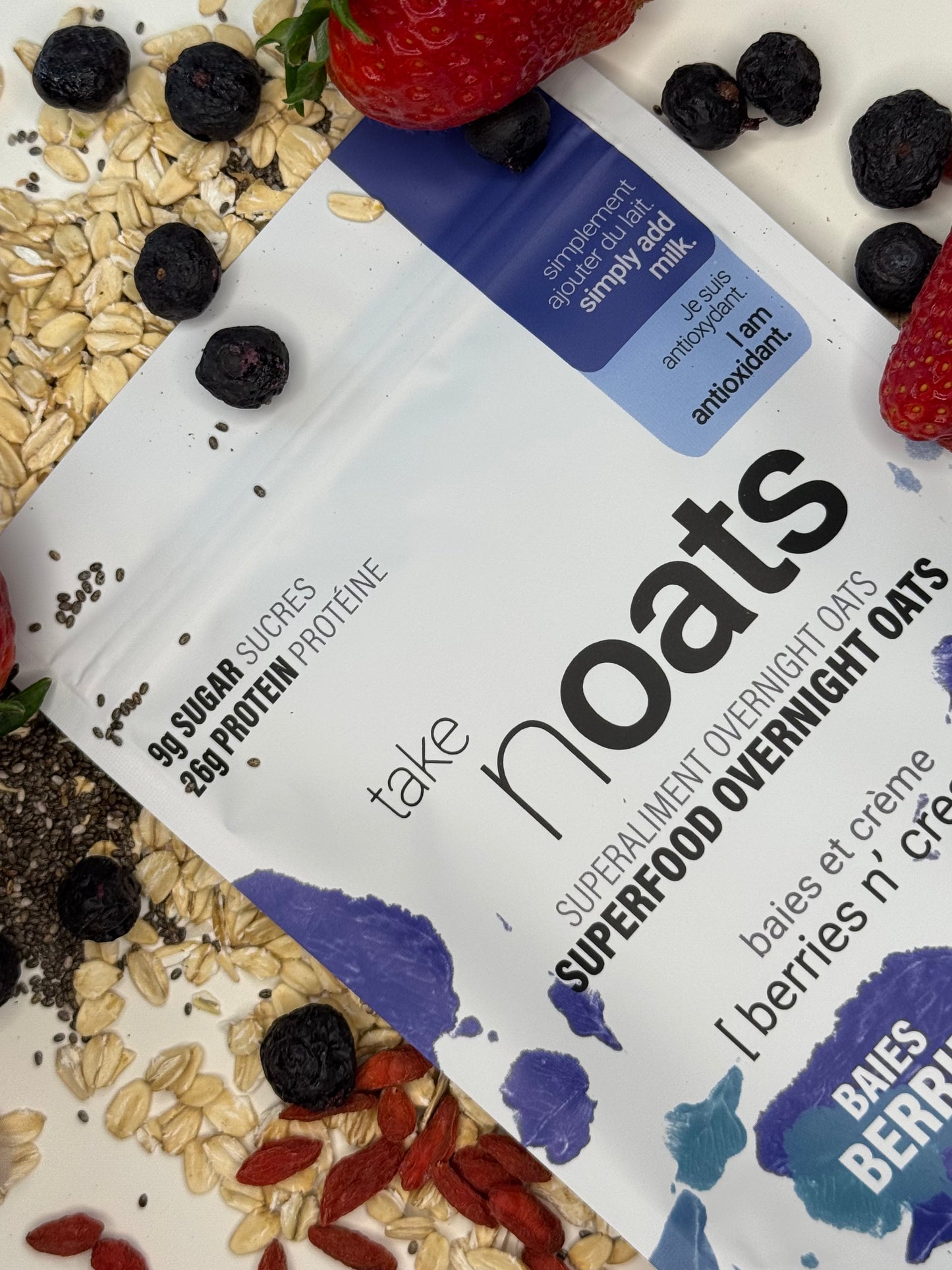 Berries n Cream Overnight Oats pouch with fresh blueberries and goji berries scattered on white background.