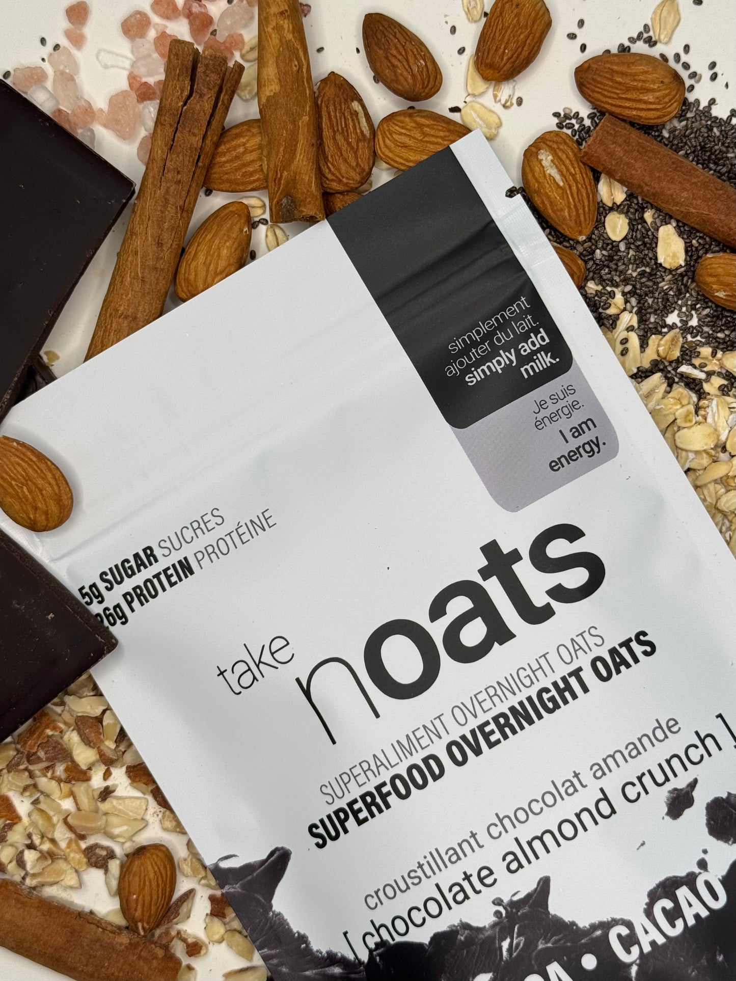 Chocolate Almond Crunch Overnight Oats pouch with dark chocolate bar pieces, almonds and rolled oats scattered on white background