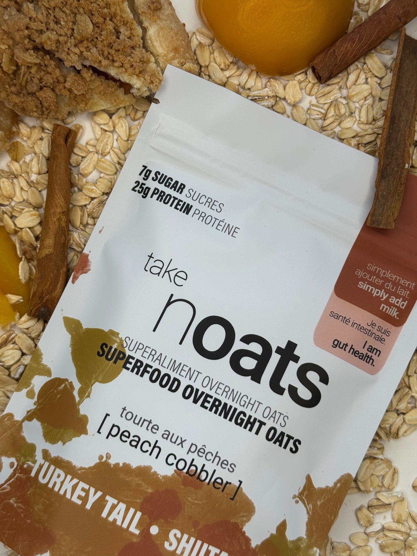 Peach Cobbler Overnight Oats pouch with peach slices and rolled oats scattered on white background.