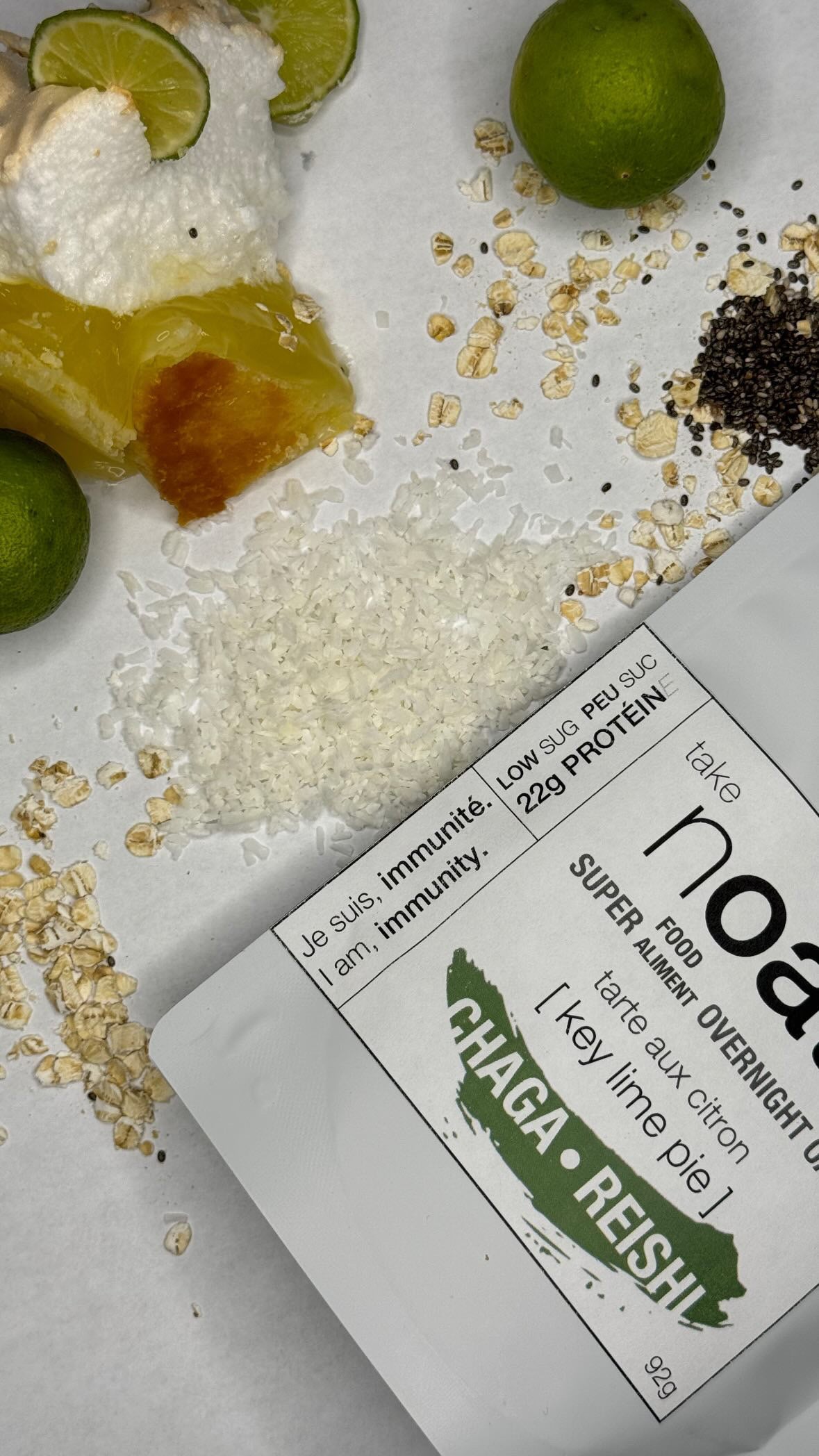 Key Lime Pie Overnight Oats pouch with lime wedges and rolled oats scattered on white background